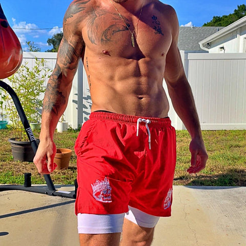 male model outside shirtless wearing red 2 in 1 hybrid shorts with compression liners from king killers apparel