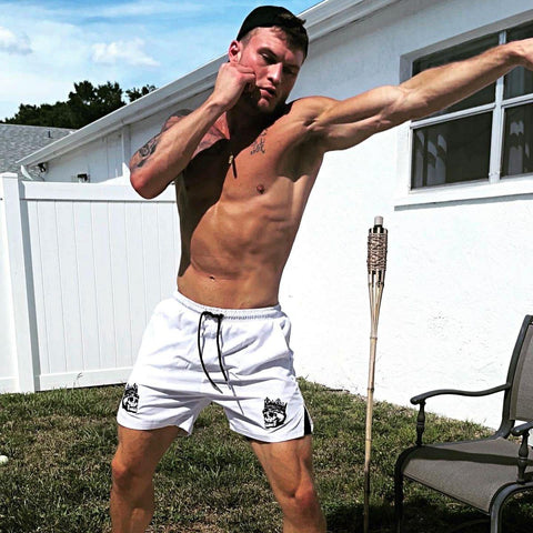 shirtless man shadowboxing outside wearing white 2 in 1 hybrid shorts with compression liners from king killers apparel