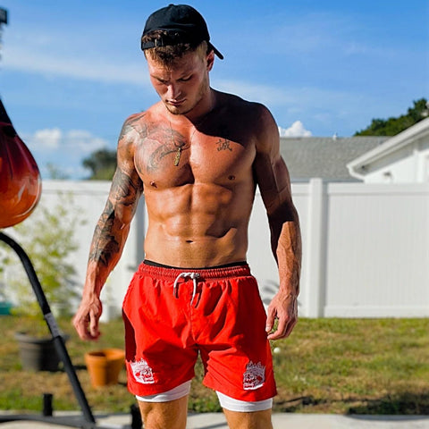shirtless male model outside wearing backwards dad hat and red 2 in 1 hybrid shorts from king killers apparel